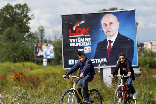 CAMPAA. Unos nios montan en bicicleta cerca de un cartel electoral en Kosovo.