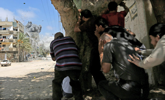 ATAQUE. Un grupo de civiles se protege detrs de un rbol mientras mira cmo los bombardeos de Israel destruyen un edificio en Gaza.